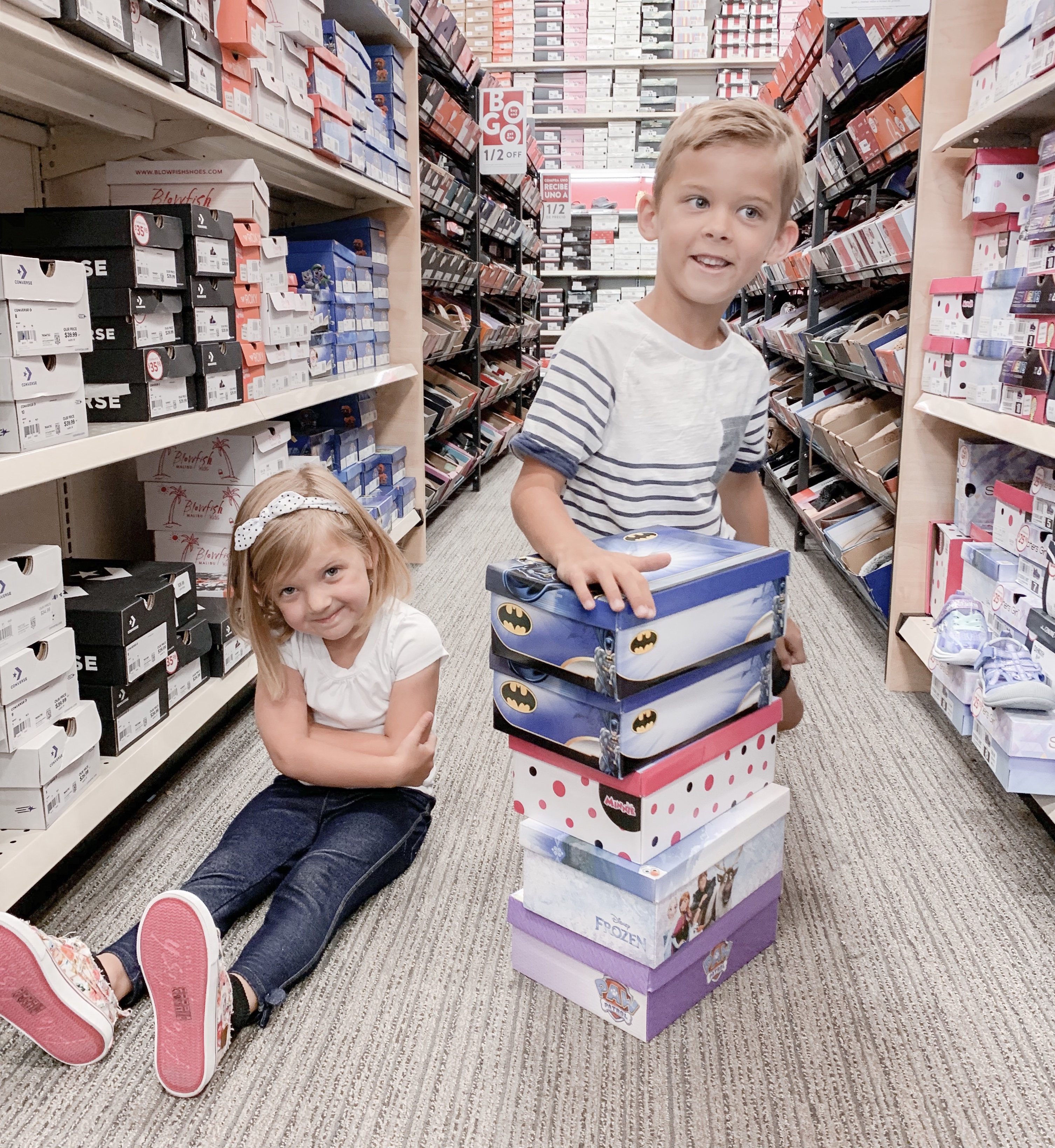 Back To School Shoes from Famous Footwear by popular San Diego fashion blog, Domestic Blonde: image of two young kids sitting in an aisle at Famous Footwear with a stacked pile of shoe boxes.