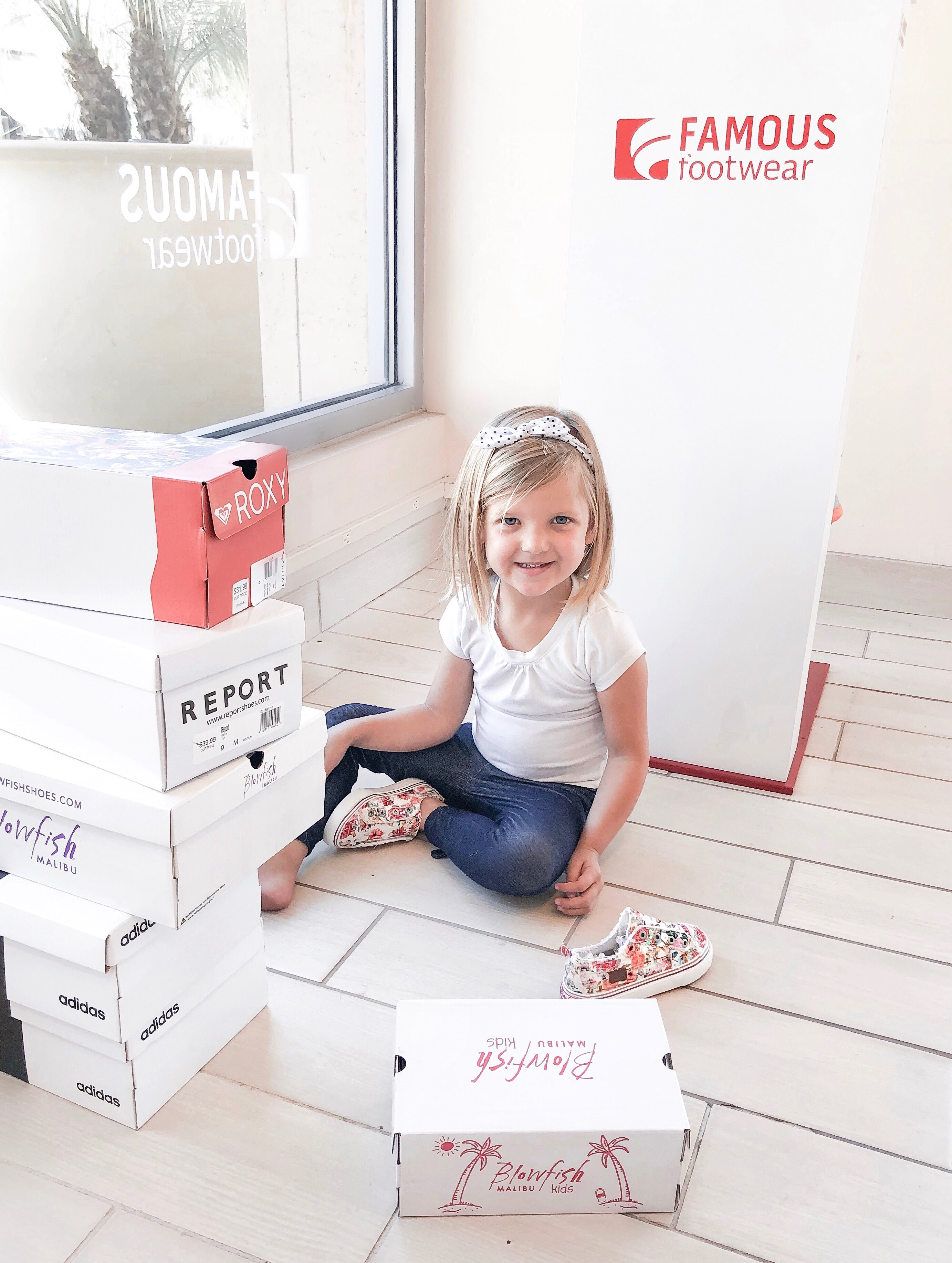 Back To School Shoes from Famous Footwear by popular San Diego fashion blog, Domestic Blonde: image of a young girl sitting on the floor at Famous Footwear surrounded by piles of stacked shoes boxes.