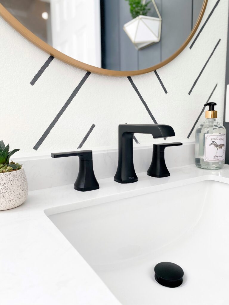 Kids Bathroom by popular San Diego interior design blog, Domestic Blonde: image of a remodeled kids bathroom with a white and grey stripe accent wall, round mirror, white vanity, and black faucet. 