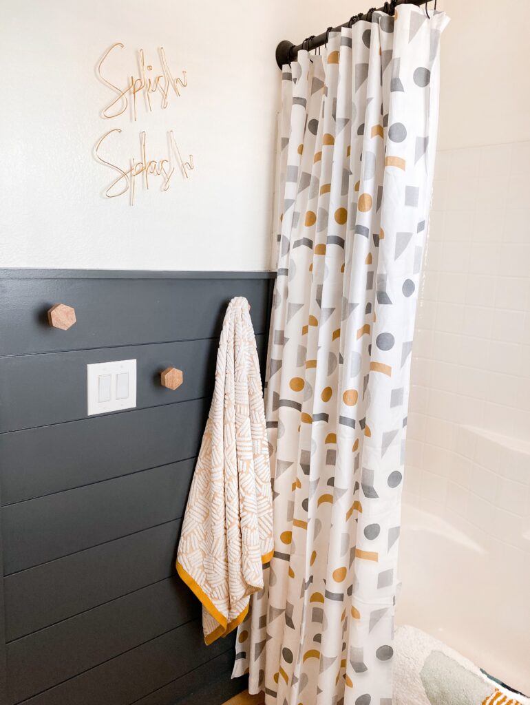 Kids Bathroom by popular San Diego interior design blog, Domestic Blonde: image of a remodeled kids bathroom with a grey shiplap wall, modern lighting, round mirror, white vanity, light wood flooring, and abstract shape shower curtain. 