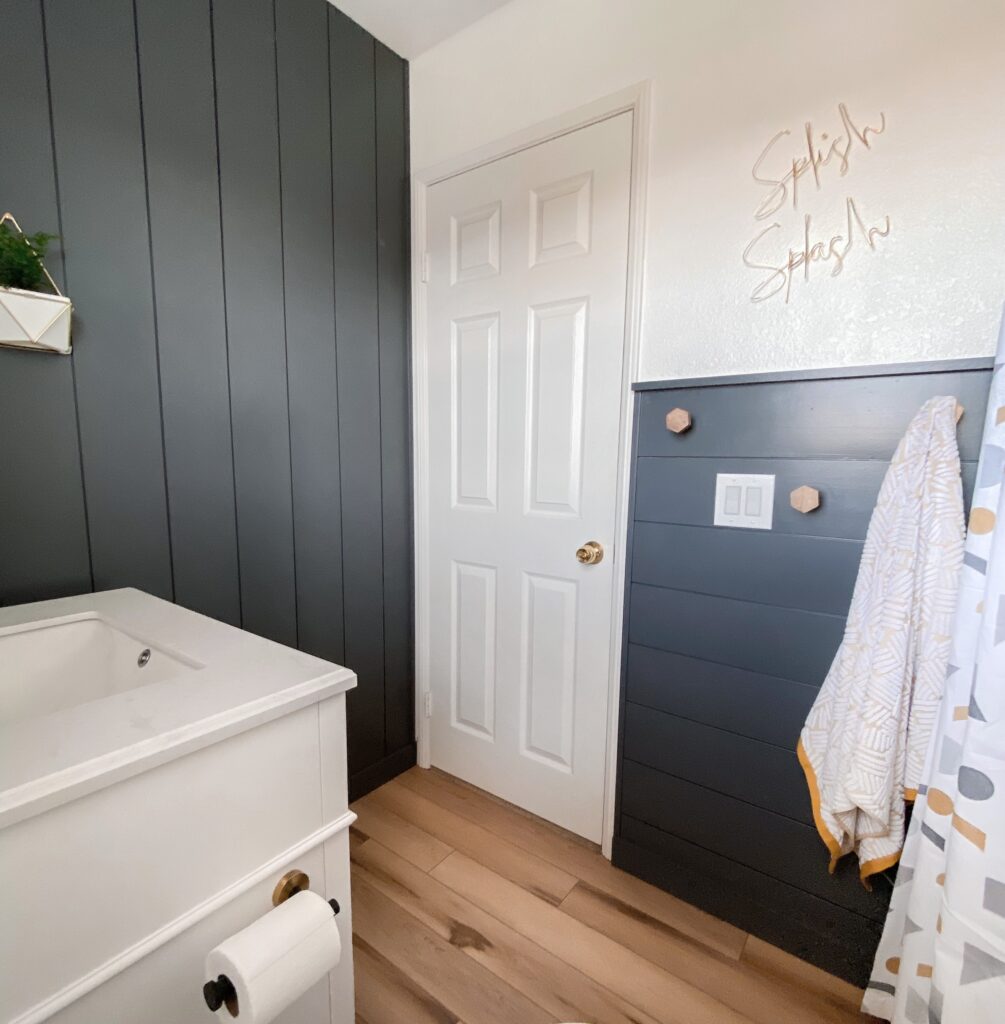 Kids Bathroom by popular San Diego interior design blog, Domestic Blonde: image of a remodeled kids bathroom with a grey shiplap wall, white vanity, light wood flooring, and abstract shape shower curtain. 