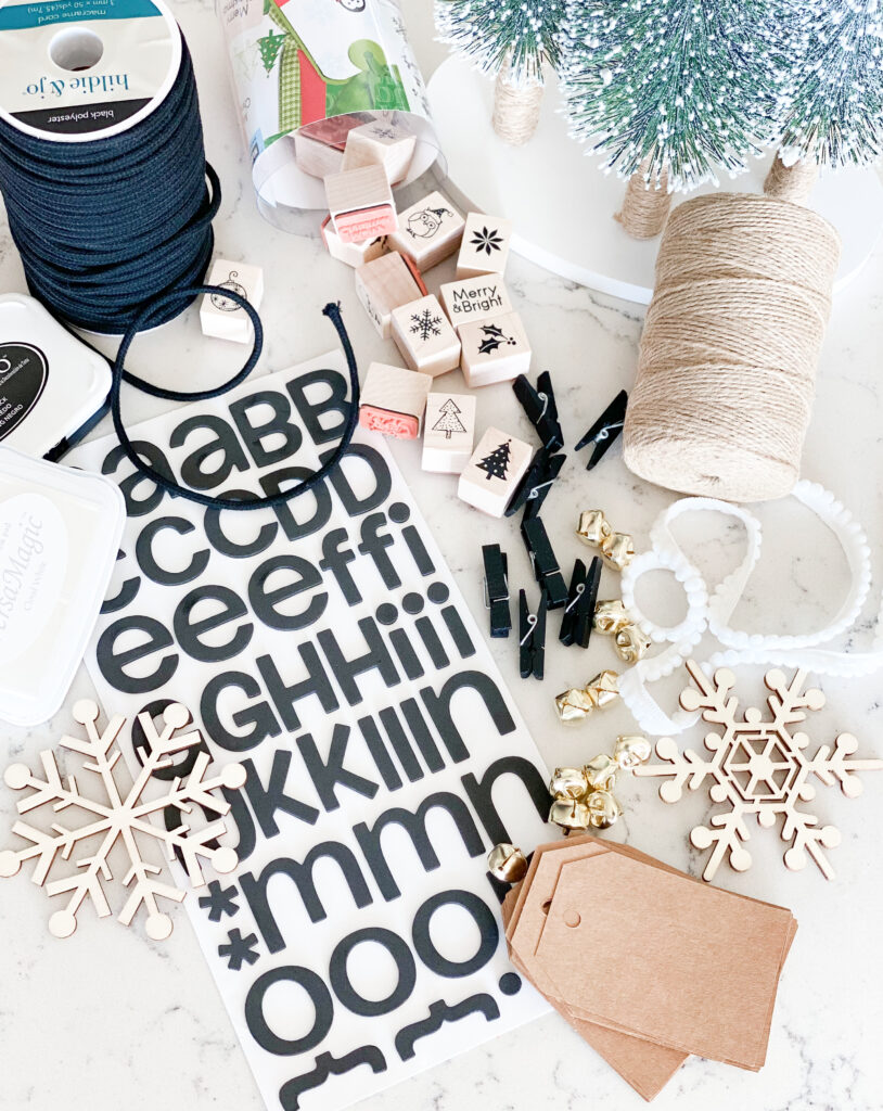 Personalized Wrapping Paper by popular San Diego DIY blog, Domestic Blonde: image of Joann's stamps, letter stickers, twine, wooden snowflakes, gift tags, gold sleigh bells, and black clothes pins. 